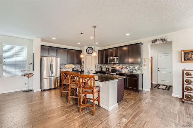 kitchen with decorative backsplash, appliances with stainless steel finishes, a kitchen breakfast bar, and a kitchen island with sink