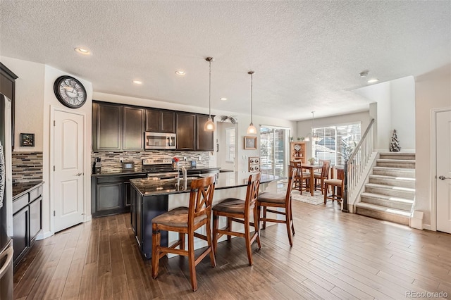 kitchen featuring an island with sink, tasteful backsplash, appliances with stainless steel finishes, a breakfast bar area, and dark wood-style flooring