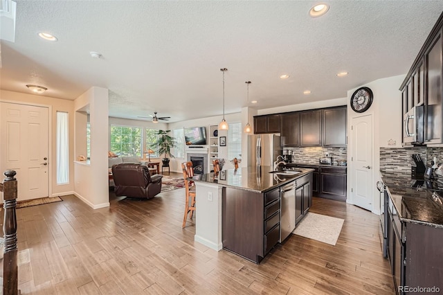 kitchen featuring a sink, open floor plan, stainless steel appliances, dark brown cabinetry, and a fireplace