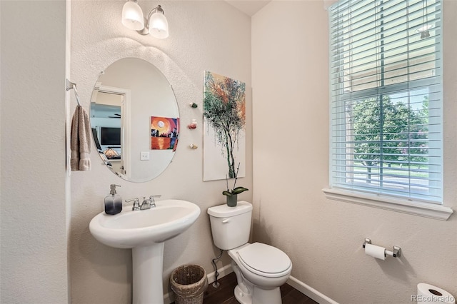 half bath with toilet, wood finished floors, and baseboards