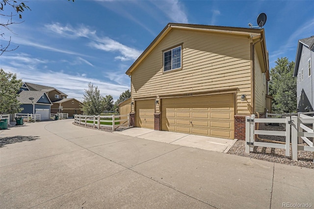 view of side of property featuring concrete driveway, an attached garage, fence, and brick siding