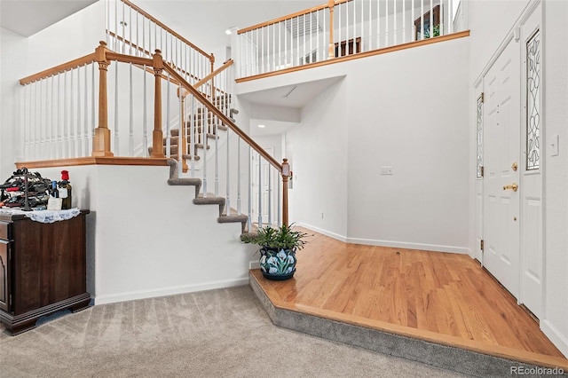 stairs featuring baseboards, wood finished floors, and a towering ceiling