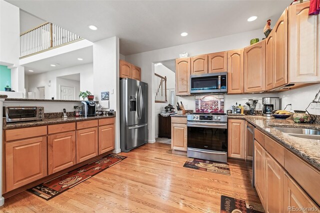 kitchen with stainless steel appliances, light wood-style floors, dark stone counters, a sink, and recessed lighting