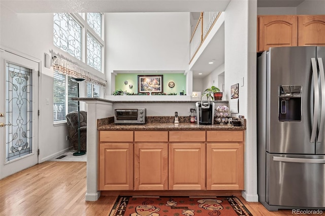 kitchen with stainless steel fridge, plenty of natural light, a towering ceiling, light wood-style flooring, and dark stone counters