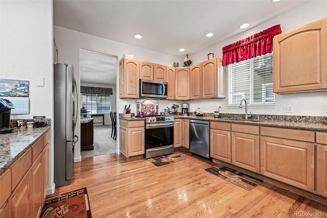 kitchen featuring appliances with stainless steel finishes, a sink, light wood-style flooring, dark stone countertops, and recessed lighting