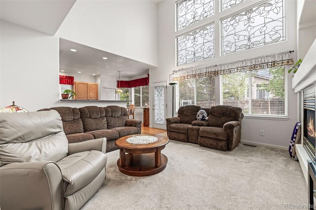 carpeted living room featuring healthy amount of natural light, a high ceiling, a glass covered fireplace, baseboards, and recessed lighting