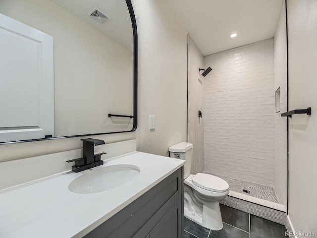 bathroom with a tile shower, vanity, tile patterned floors, and toilet