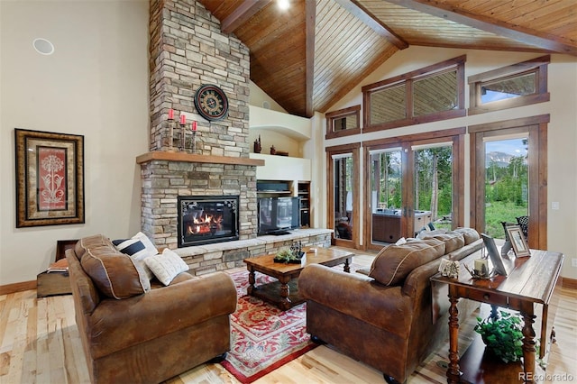 living room with beam ceiling, wood ceiling, a stone fireplace, and light wood-type flooring