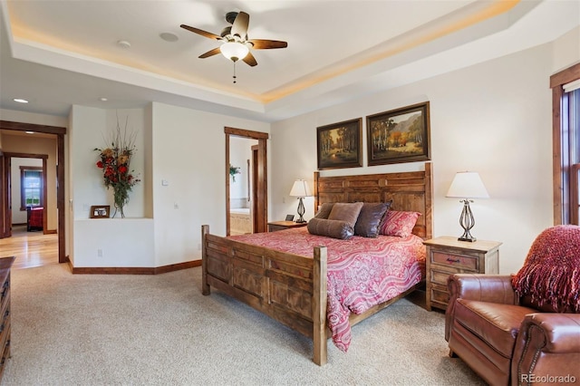 bedroom featuring ensuite bathroom, light carpet, ceiling fan, and a tray ceiling