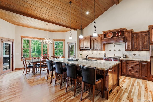 kitchen featuring a kitchen island with sink, sink, pendant lighting, and light stone counters