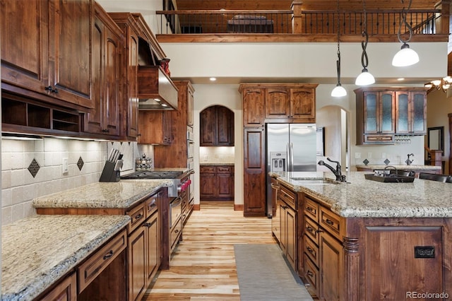 kitchen featuring sink, light hardwood / wood-style flooring, hanging light fixtures, a towering ceiling, and a center island with sink