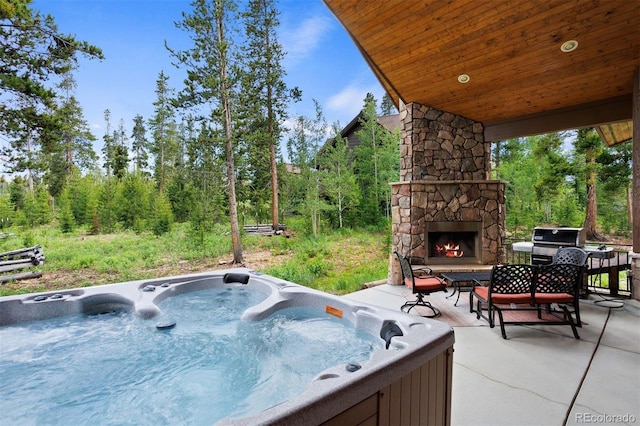 view of patio with a grill, a hot tub, and an outdoor stone fireplace