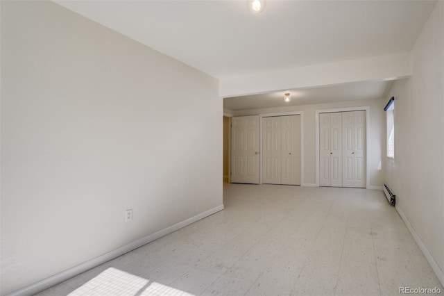 unfurnished bedroom with baseboards, a baseboard heating unit, two closets, and tile patterned floors