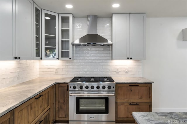 kitchen with backsplash, wall chimney range hood, high end stainless steel range, light stone countertops, and white cabinetry