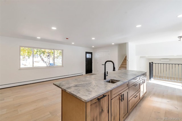 kitchen featuring light stone countertops, sink, a baseboard radiator, light hardwood / wood-style floors, and a kitchen island with sink