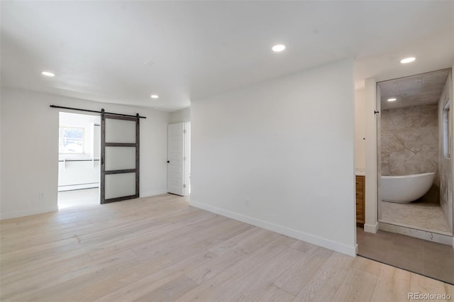 empty room with a barn door, light hardwood / wood-style floors, and a baseboard heating unit