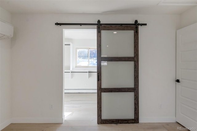 spare room with a barn door, light wood-type flooring, an AC wall unit, and a baseboard radiator