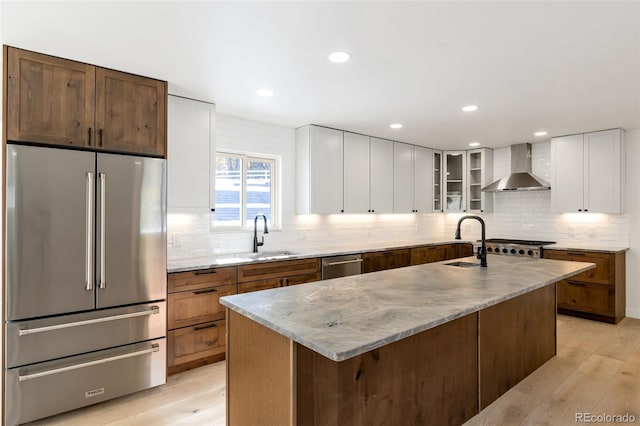 kitchen with a center island with sink, wall chimney exhaust hood, white cabinetry, and appliances with stainless steel finishes