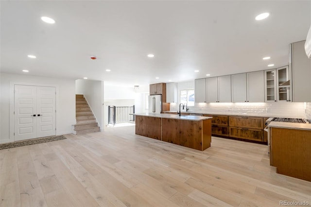 kitchen featuring tasteful backsplash, high quality fridge, a center island with sink, light hardwood / wood-style flooring, and white cabinetry