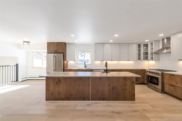 kitchen with wall chimney exhaust hood, sink, high quality appliances, white cabinets, and an island with sink