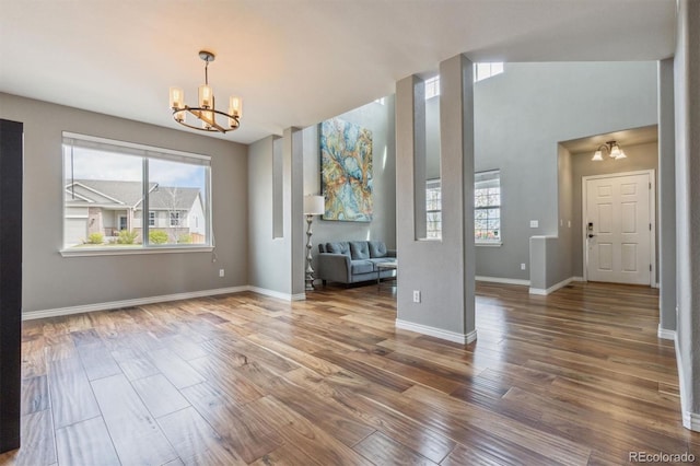 unfurnished living room with an inviting chandelier, baseboards, and wood finished floors