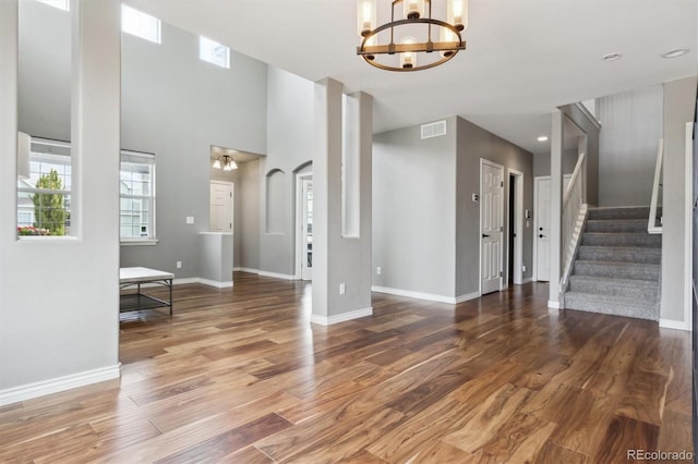 entrance foyer with a notable chandelier, stairs, baseboards, wood finished floors, and visible vents