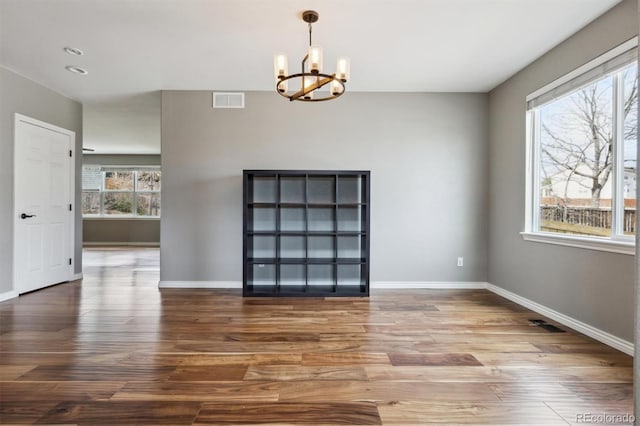 unfurnished dining area featuring visible vents, baseboards, wood finished floors, and a chandelier