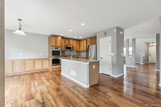kitchen with a sink, appliances with stainless steel finishes, wood finished floors, and light countertops