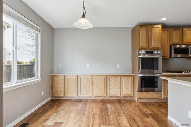 kitchen with light countertops, hanging light fixtures, stainless steel appliances, and light wood finished floors