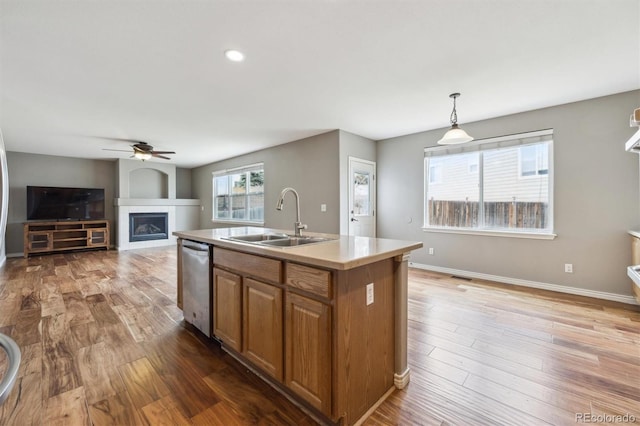 kitchen with stainless steel dishwasher, brown cabinetry, a fireplace, light countertops, and a sink