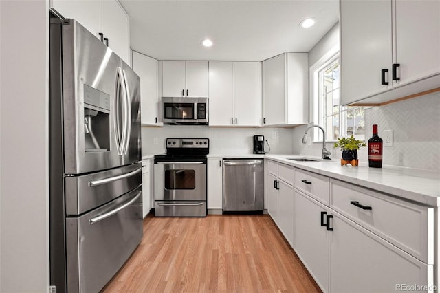 kitchen featuring white cabinets, sink, light wood-type flooring, appliances with stainless steel finishes, and light stone counters