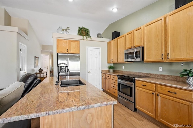 2169 Fox Fire St, Highlands Ranch, CO 80129 - kitchen featuring appliances with stainless steel finishes, vaulted ceiling, light wood-style flooring, a center island with sink, and light stone counters