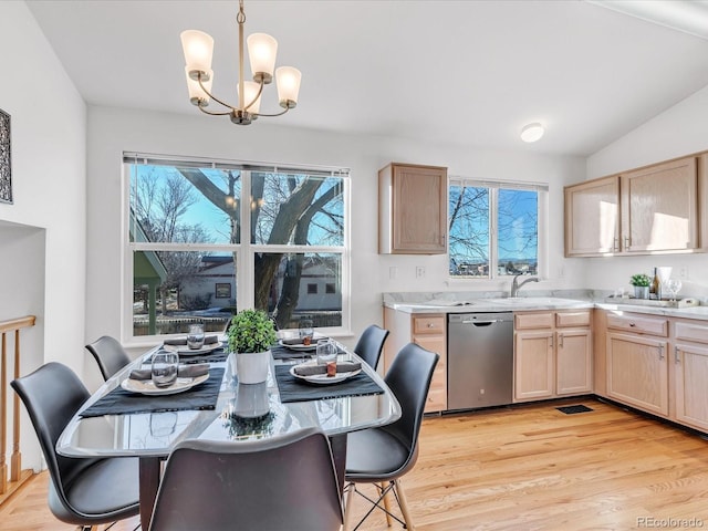 dining space with light wood-type flooring, an inviting chandelier, vaulted ceiling, and sink