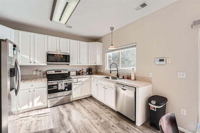 kitchen featuring light wood-type flooring, stainless steel appliances, sink, white cabinets, and hanging light fixtures