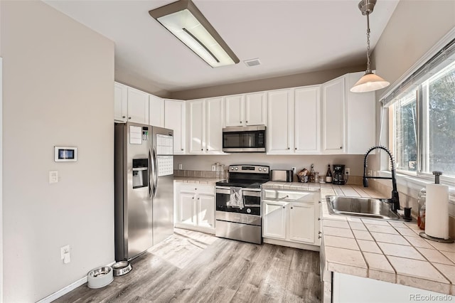 kitchen with sink, appliances with stainless steel finishes, decorative light fixtures, light hardwood / wood-style floors, and white cabinetry