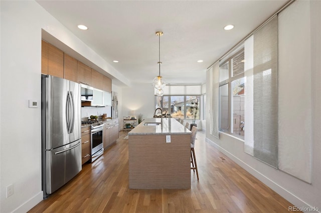 kitchen featuring appliances with stainless steel finishes, pendant lighting, sink, a kitchen breakfast bar, and a kitchen island with sink