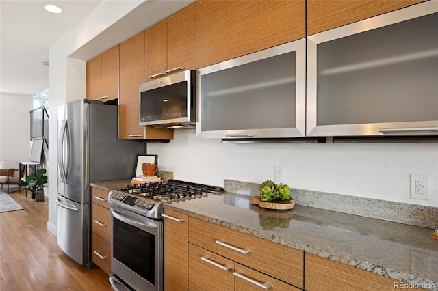 kitchen with light stone countertops, appliances with stainless steel finishes, and light hardwood / wood-style floors