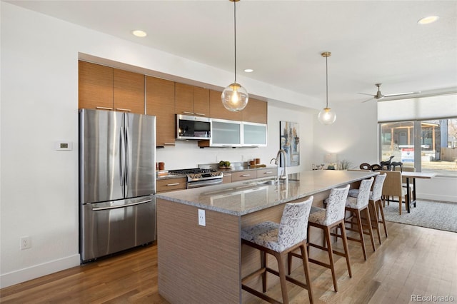 kitchen featuring wood finished floors, appliances with stainless steel finishes, a sink, and brown cabinets