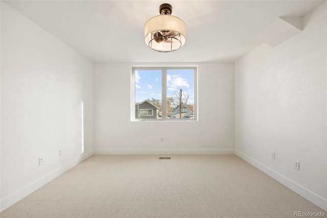 spare room featuring light colored carpet, visible vents, and baseboards