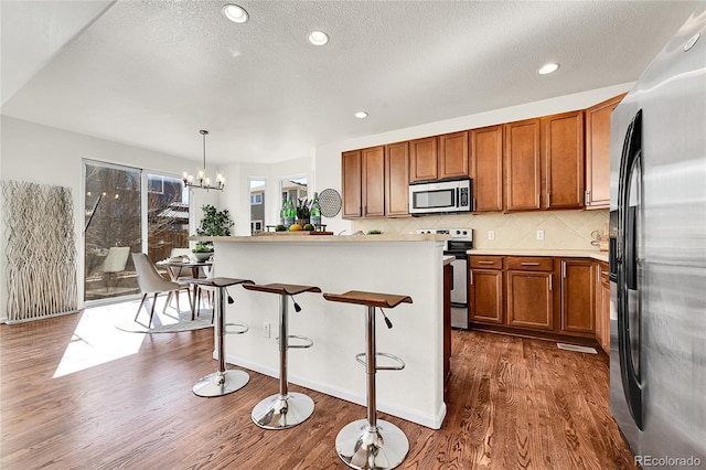 kitchen with dark wood-style flooring, brown cabinets, light countertops, backsplash, and appliances with stainless steel finishes