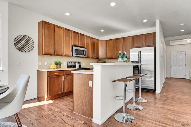 kitchen featuring stainless steel appliances, light countertops, brown cabinetry, light wood-type flooring, and a kitchen breakfast bar