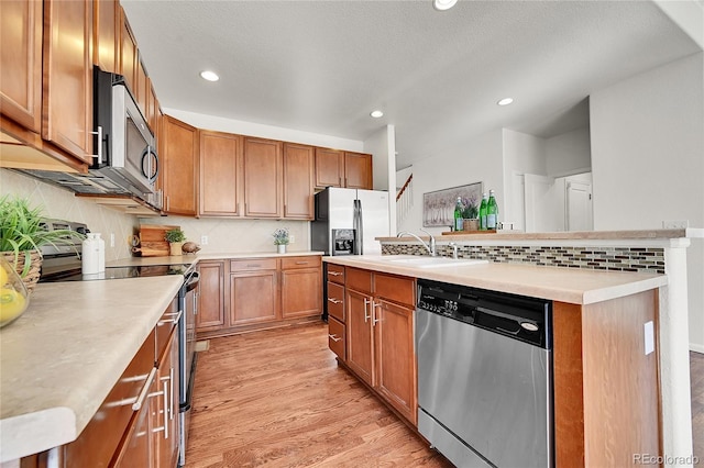 kitchen featuring stainless steel appliances, a sink, light countertops, light wood finished floors, and an island with sink