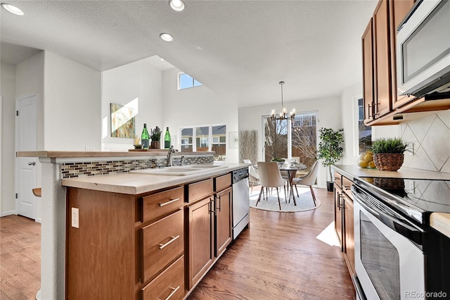 kitchen featuring a sink, appliances with stainless steel finishes, brown cabinets, light wood finished floors, and a center island with sink