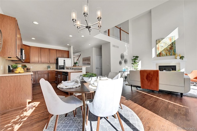 dining space with recessed lighting, a notable chandelier, dark wood finished floors, visible vents, and a glass covered fireplace