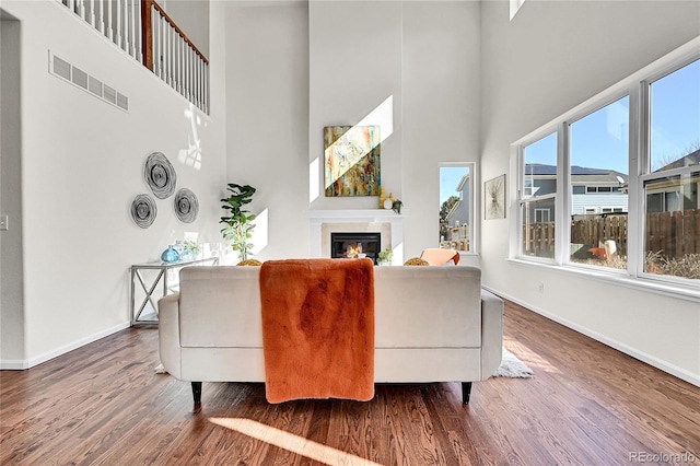 living area featuring wood finished floors, a glass covered fireplace, visible vents, and baseboards