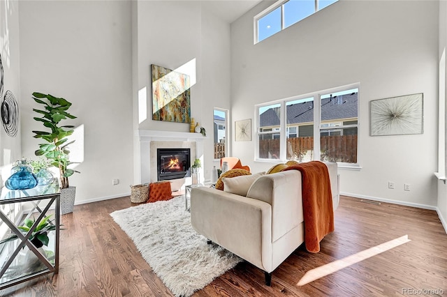 living area with a towering ceiling, baseboards, wood finished floors, and a glass covered fireplace