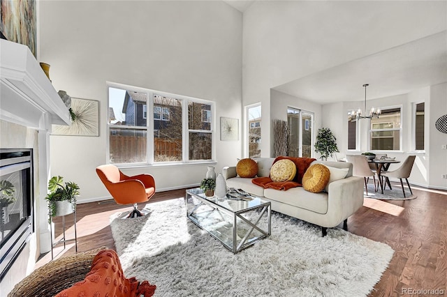 living room featuring a chandelier, a high ceiling, wood finished floors, baseboards, and a glass covered fireplace