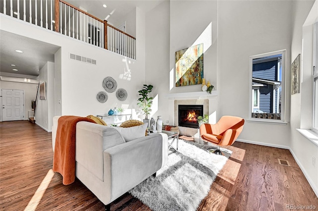 living area featuring baseboards, a tiled fireplace, visible vents, and wood finished floors