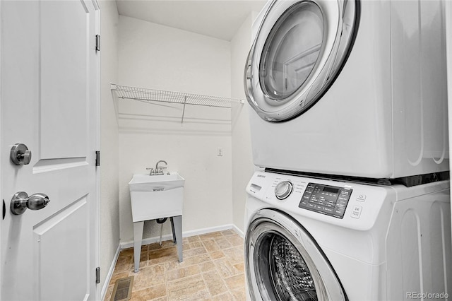 clothes washing area featuring visible vents, stone finish floor, stacked washing maching and dryer, laundry area, and baseboards