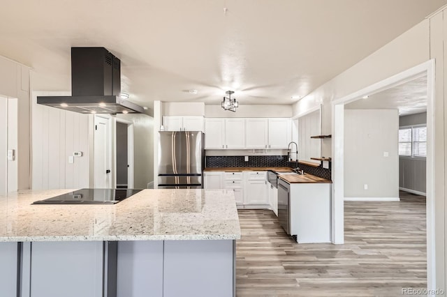 kitchen with island range hood, white cabinets, a sink, light wood-style flooring, and stainless steel appliances